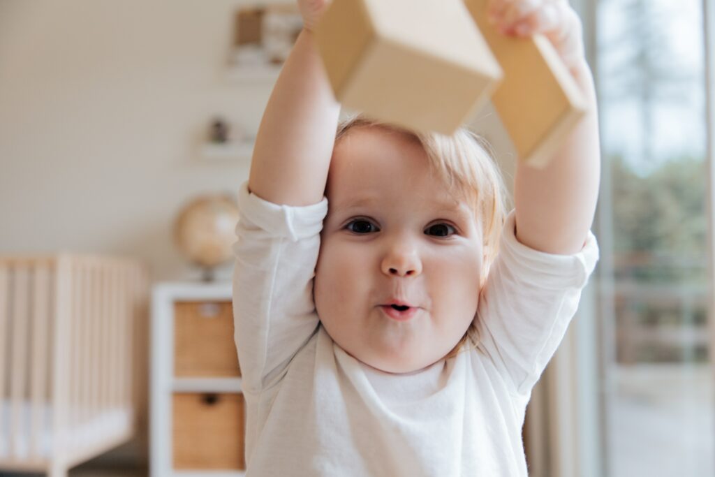 Baby in white onesie playing with wooden blocks.